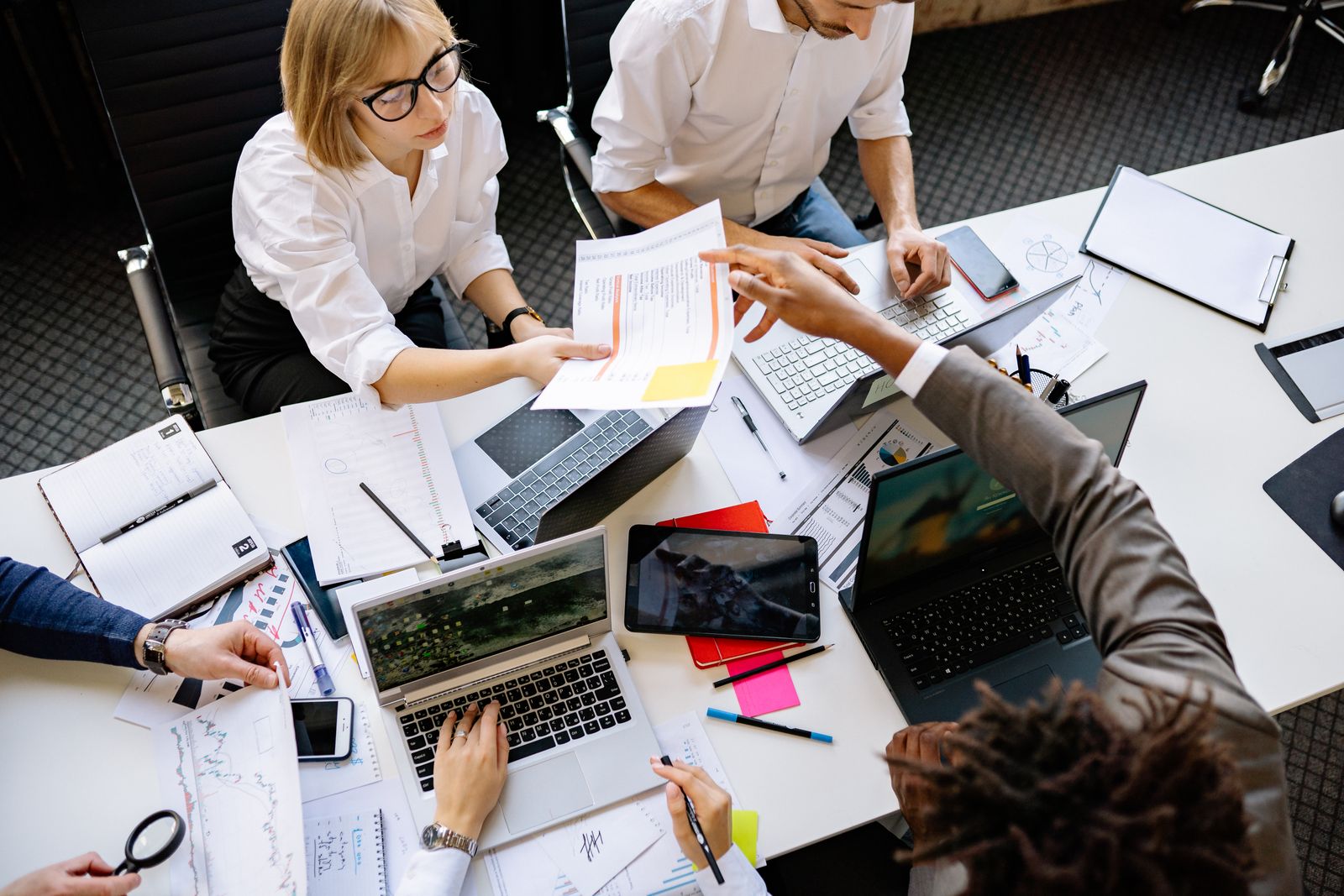 Diverse revenue team working together at a desk with laptops and documents, illustrating a team combining multiple intent signals to score a warm account.